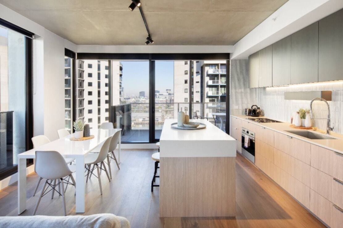 Eine moderne Küche mit einer zentralen Kochinsel, einem Essbereich mit weißem Tisch und Stühlen sowie großen Fenstern mit Blick auf die Stadt.