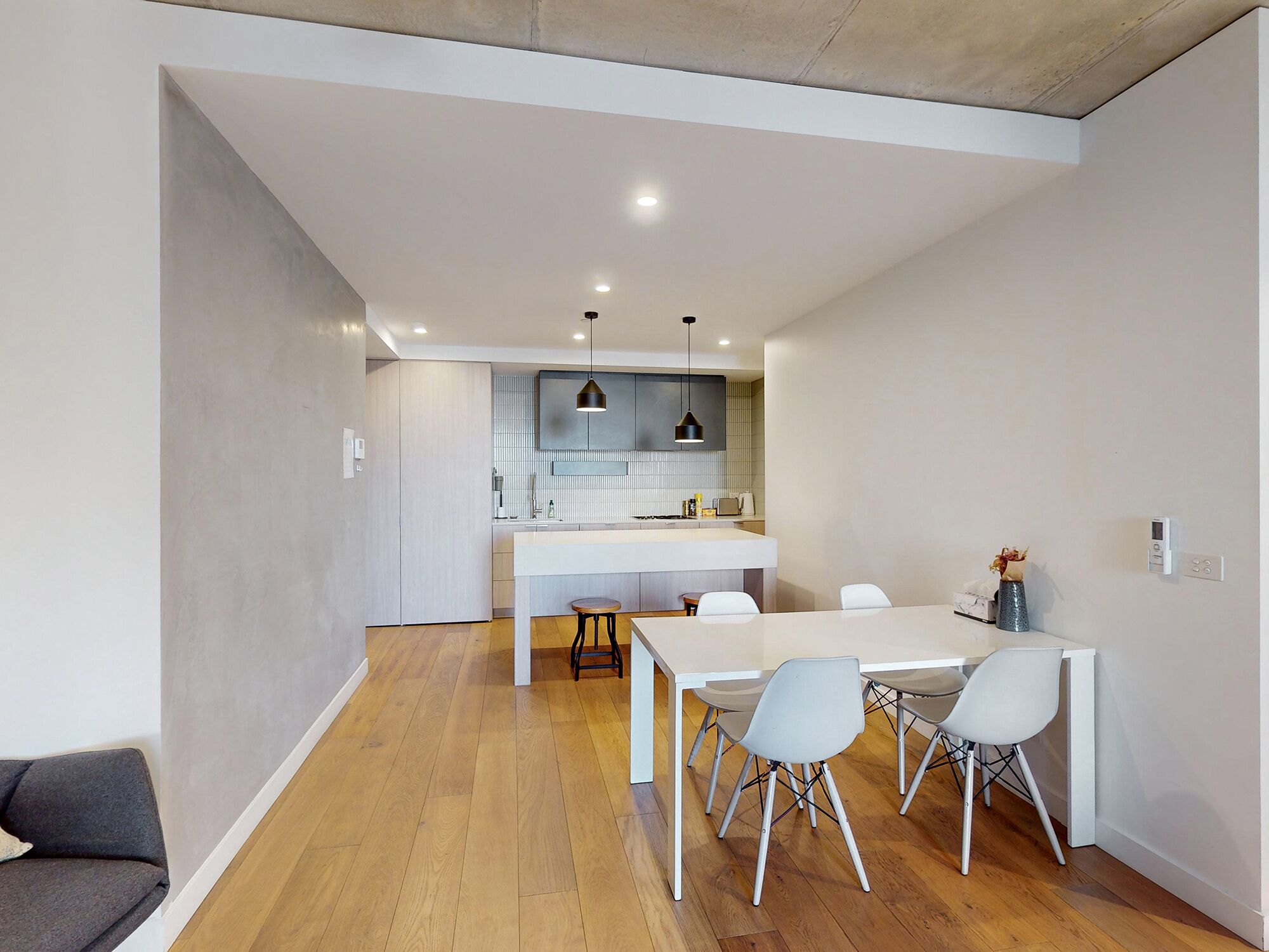 Una cocina moderna con una isla central, iluminación colgante y una zona de comedor con mesa y sillas blancas.