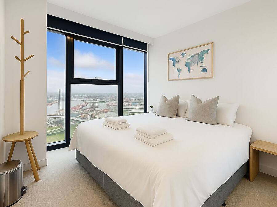 Habitación de hotel moderna con una cama grande, vista panorámica de la ciudad a través de un ventanal de pared a techo, un perchero y una mesita de noche.