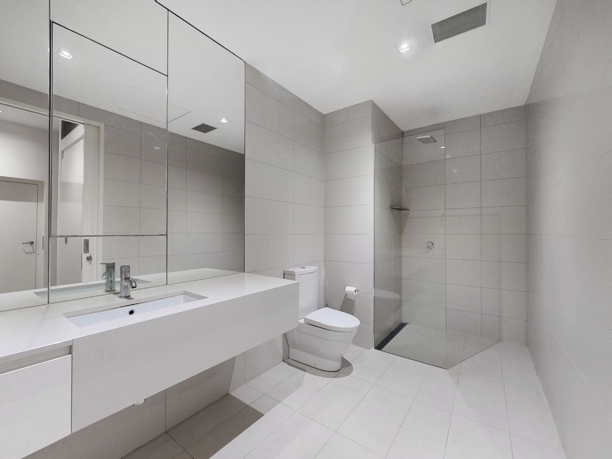 Une salle de bain moderne avec un grand miroir, un lavabo blanc et une douche à l’italienne.