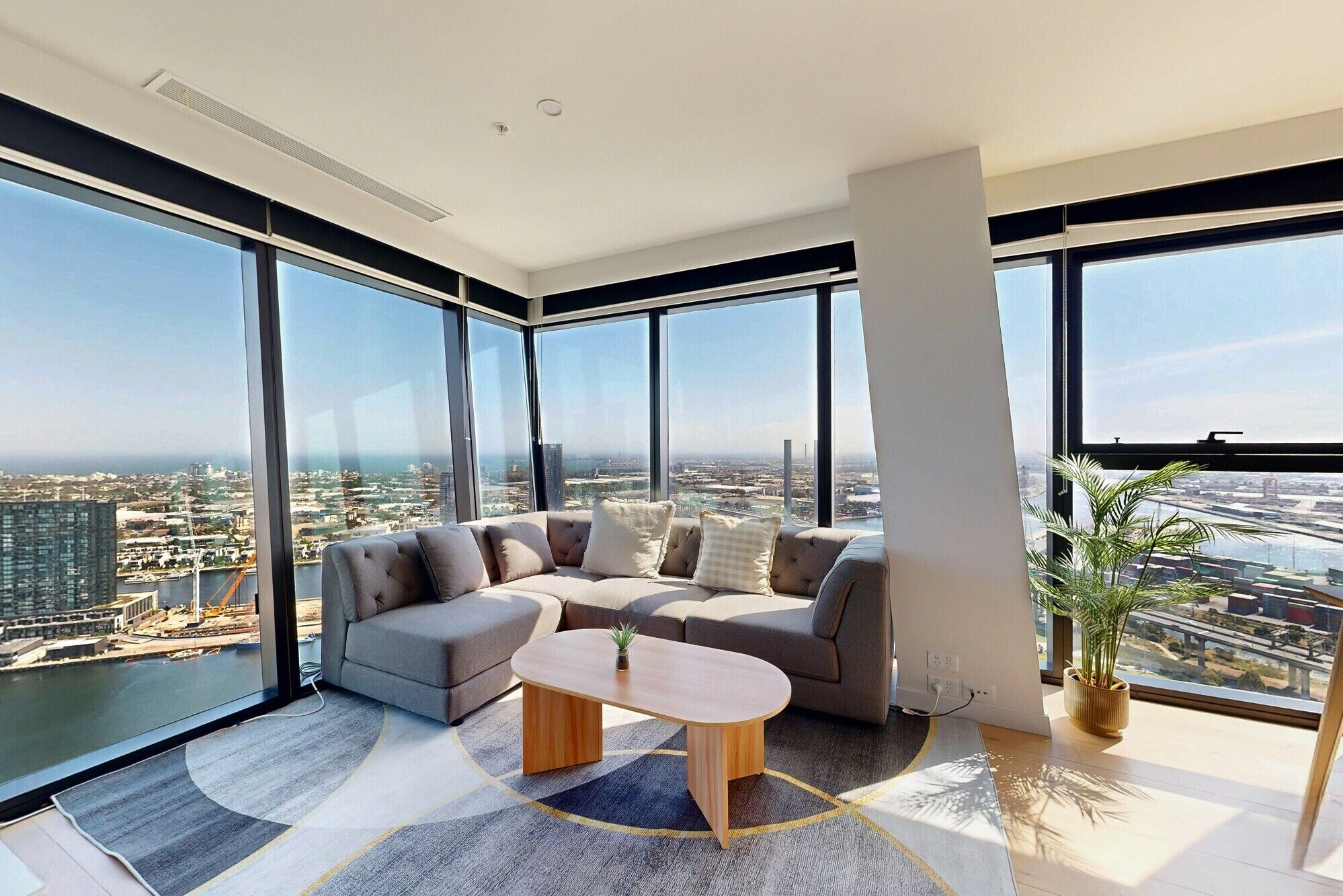 A modern living room with a curved sofa, a wooden coffee table, and large floor-to-ceiling windows offering a city view.