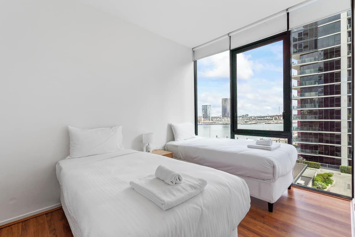 A modern hotel room with two beds, large windows, and a view of the city.
