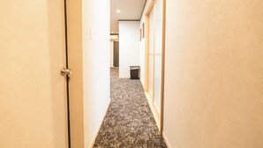 A narrow hallway with carpeted flooring, a trash bin, and a door on the left. - b&Kuromon (Osaka)