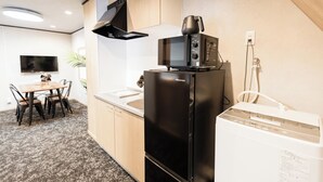 A compact kitchen with a black refrigerator, a microwave, and a small sink. There is a dining table with chairs and a plant in the background. - b&Kuromon (Osaka)