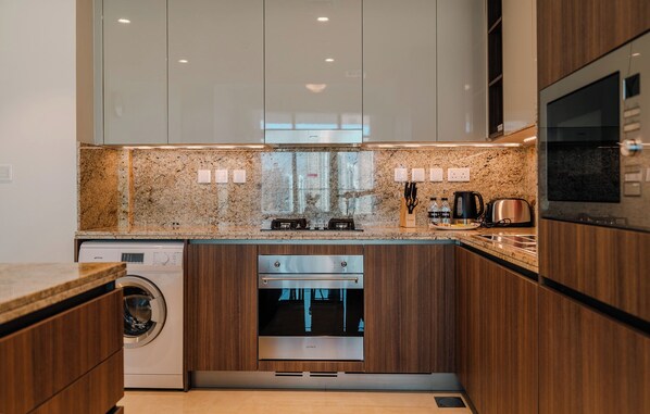 A modern kitchen with granite countertops, stainless steel appliances, and wooden cabinetry. - Imperial Avenue Residences - Downtown (Dubai)