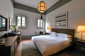 A hotel room with a large bed, a desk with a chair, a small table, a lamp, and a telephone. - LeeManorHotel (Xiamen)