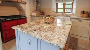 Una cucina con piano cottura rosso, piani di lavoro in granito, una ciotola di frutta e una finestra vista.