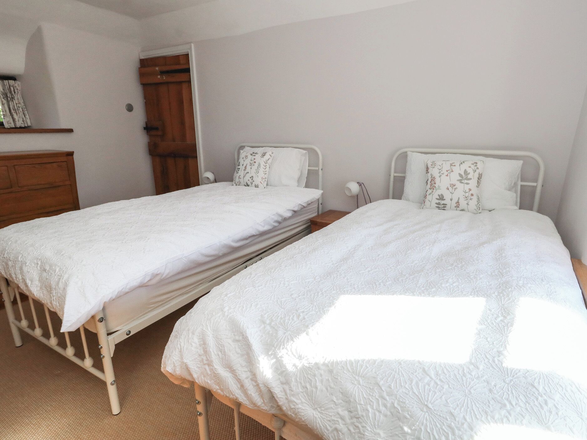 Two twin beds with white bedding in a room with a wooden wardrobe and a door.