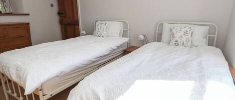 Two twin beds with white bedding in a room with a wooden wardrobe and a door.