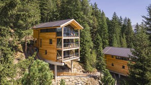 Une cabane en bois dotée d’un balcon en verre, entourée d’une forêt dense.