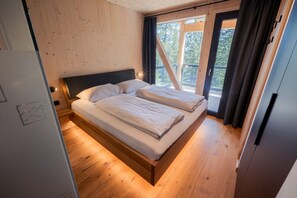 Une chambre à coucher aux murs lambrissés, avec un lit, une fenêtre avec des rideaux et une vue sur les arbres.