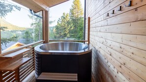 Een houten chalet met een jacuzzi, grote ramen en uitzicht op een bos.