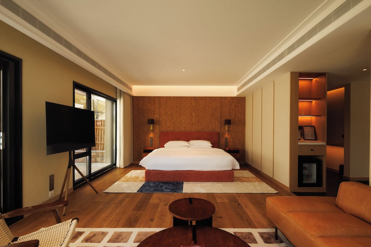 A hotel room with a large bed, a TV, a sofa, and a small table.