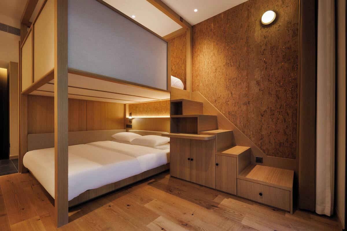 A modern bedroom with a bunk bed, wooden flooring, built-in shelving, and a staircase.