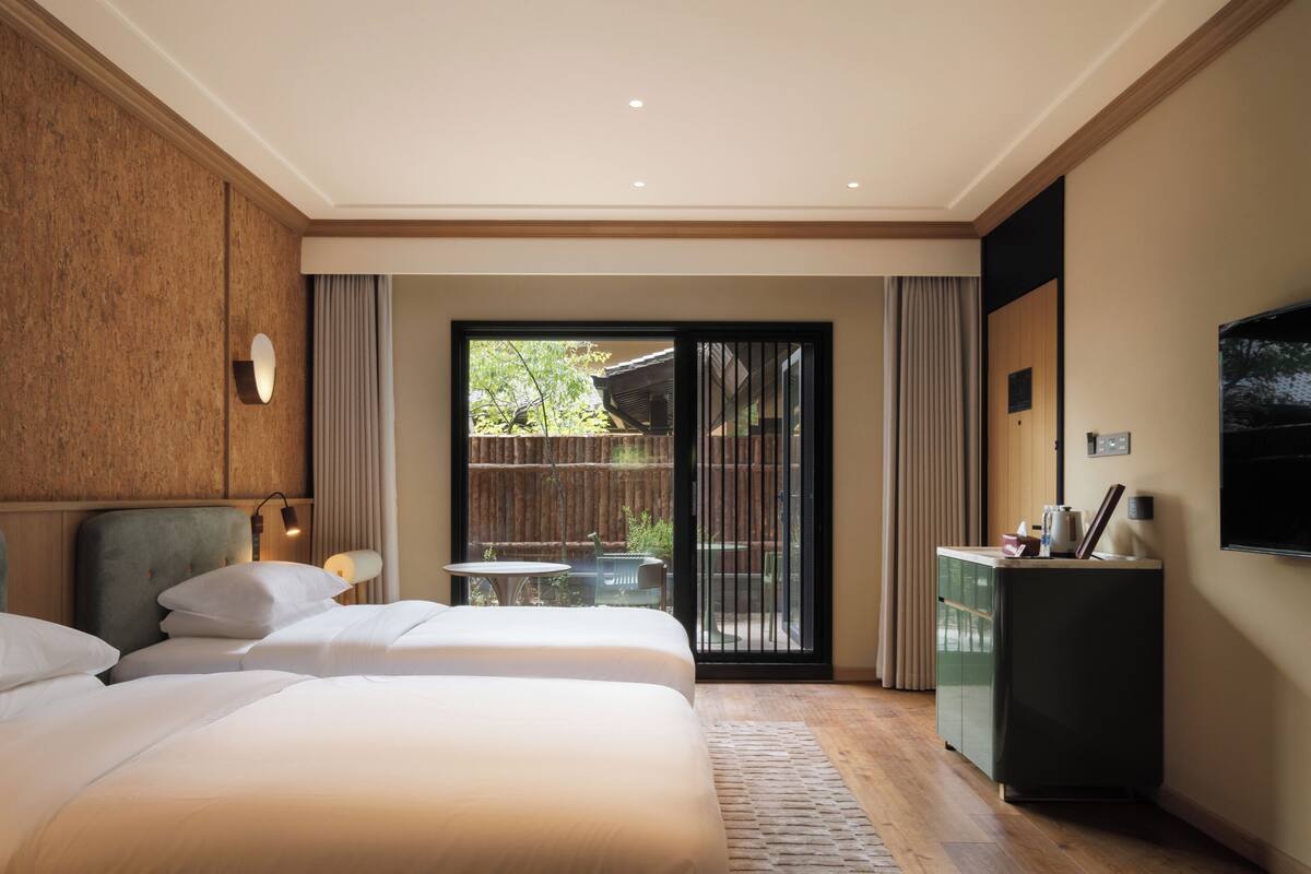A hotel room with two beds, a desk, a TV, and a sliding glass door to the outside.