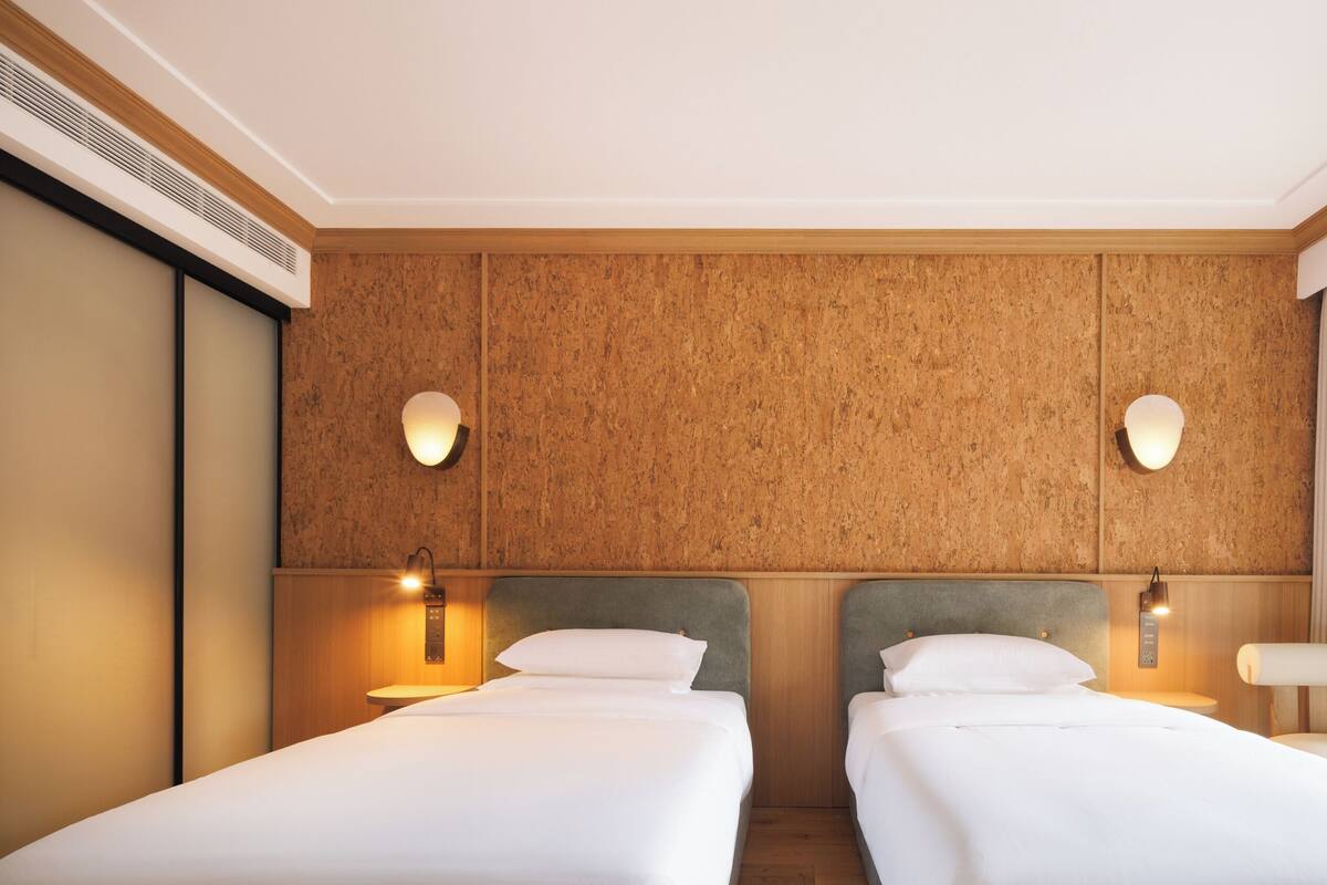 A hotel room with two single beds, a wooden panel wall, and a small table.