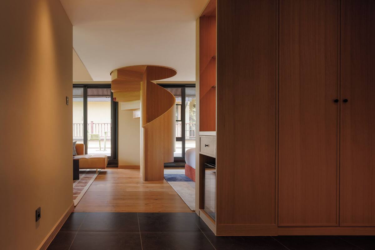 A modern interior with a spiral staircase, wooden flooring, and a view to an outdoor balcony.