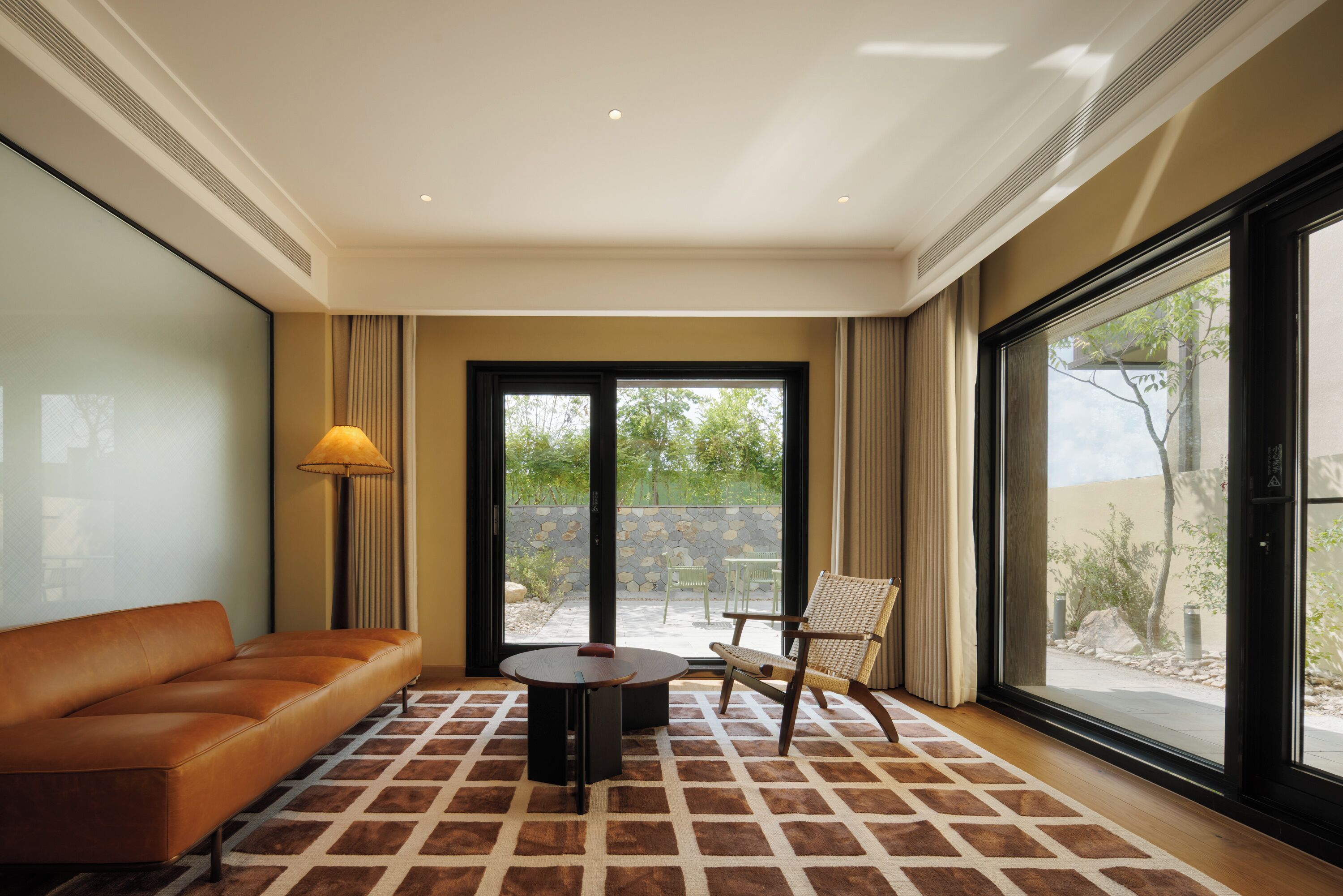 Une pièce moderne avec un canapé en cuir marron, une table ronde et une chaise dont le dossier est en osier tressé.