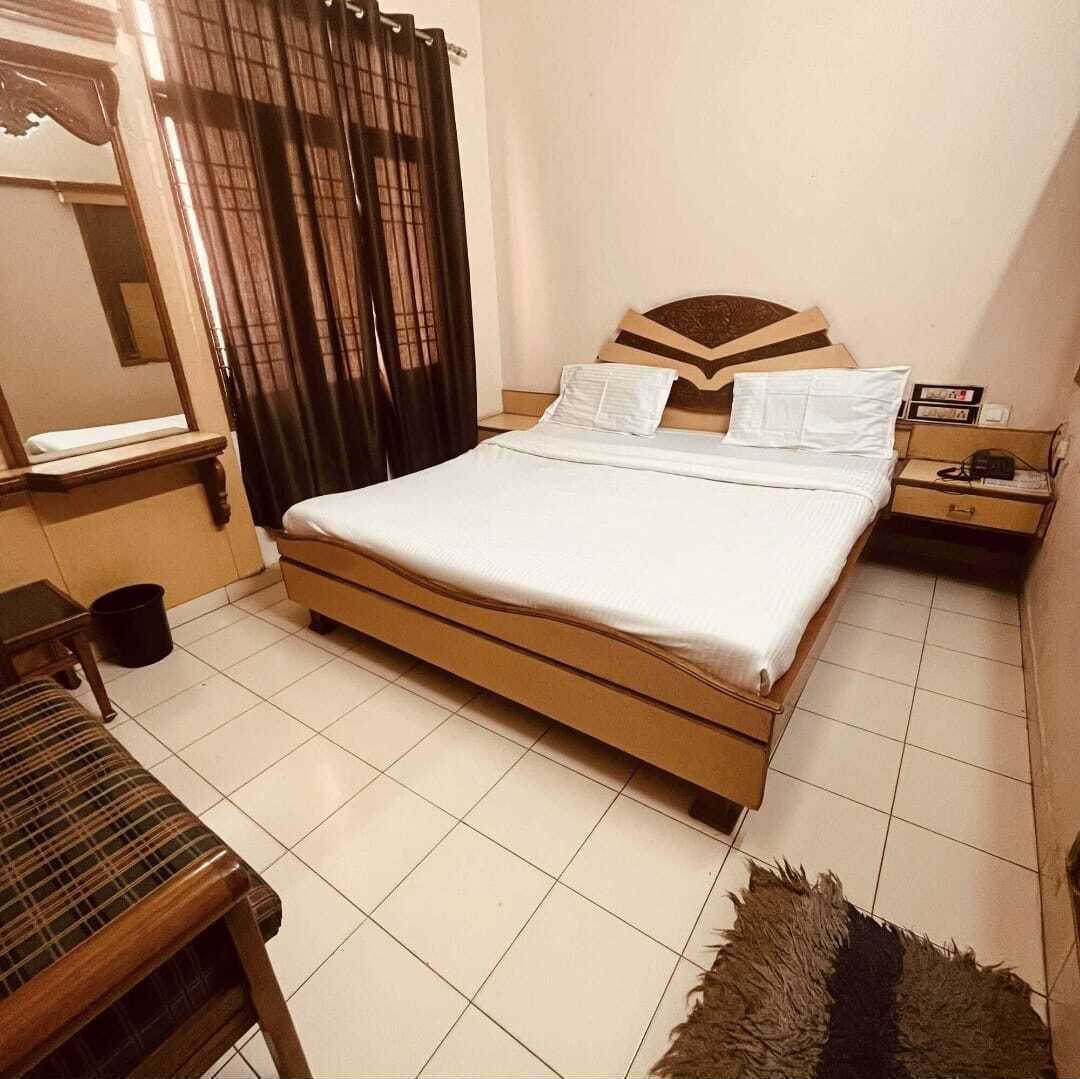 Een slaapkamer met een bed, nachtkastje, stoel en raam met gordijnen.