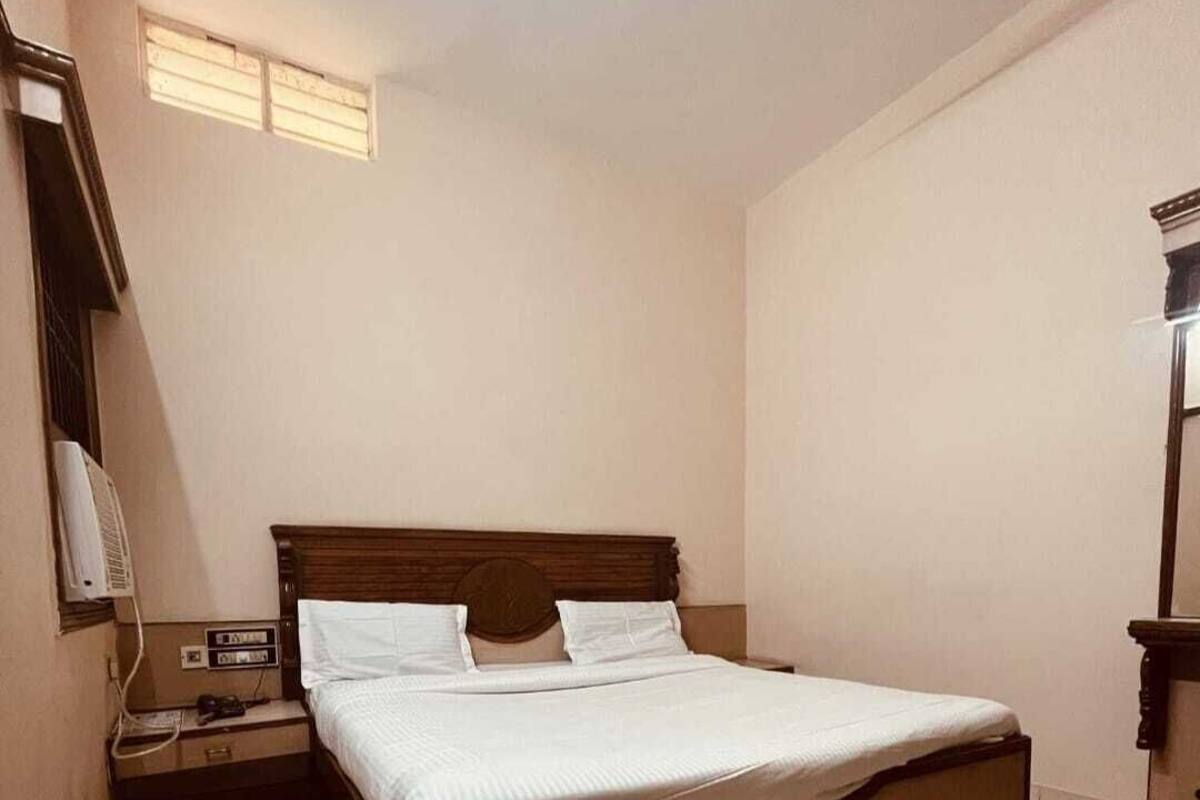 Un dormitorio con una cama de madera, una mesita de noche, un ventilador de pared y una ventana con persianas.