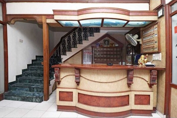 A reception desk with a curved design, a staircase with a railing, and a wall-mounted display case. - Hotel Saiom Palace (Raipur)