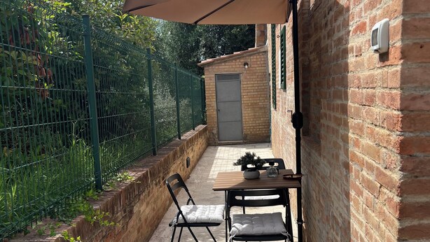 A small outdoor patio with a table and chairs, a brick wall, and a green fence.