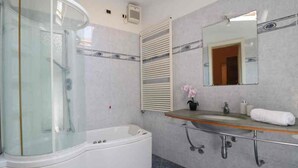 A modern bathroom with a glass-enclosed shower, a white bathtub, a vanity with a mirror, and a sink.