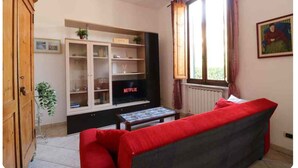 A living room with a red sofa, a TV on a stand, wooden cabinets, and a window with curtains.