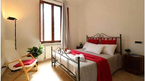 A bedroom with a bed, a chair, a window, and a bedside table.