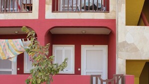 Um edifício de dois andares com fachada vermelha, uma varanda com grades e uma porta com o número 18.