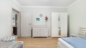 A bedroom with a bed, a dresser, a wardrobe, a chair, a small table, and a wall clock.