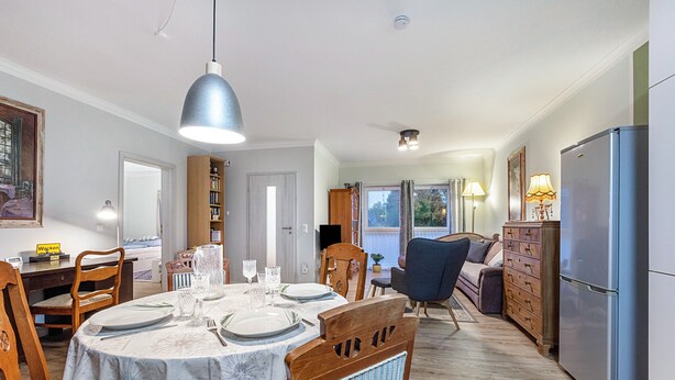 A dining area with a round table set for four, a wooden cabinet, and a refrigerator.