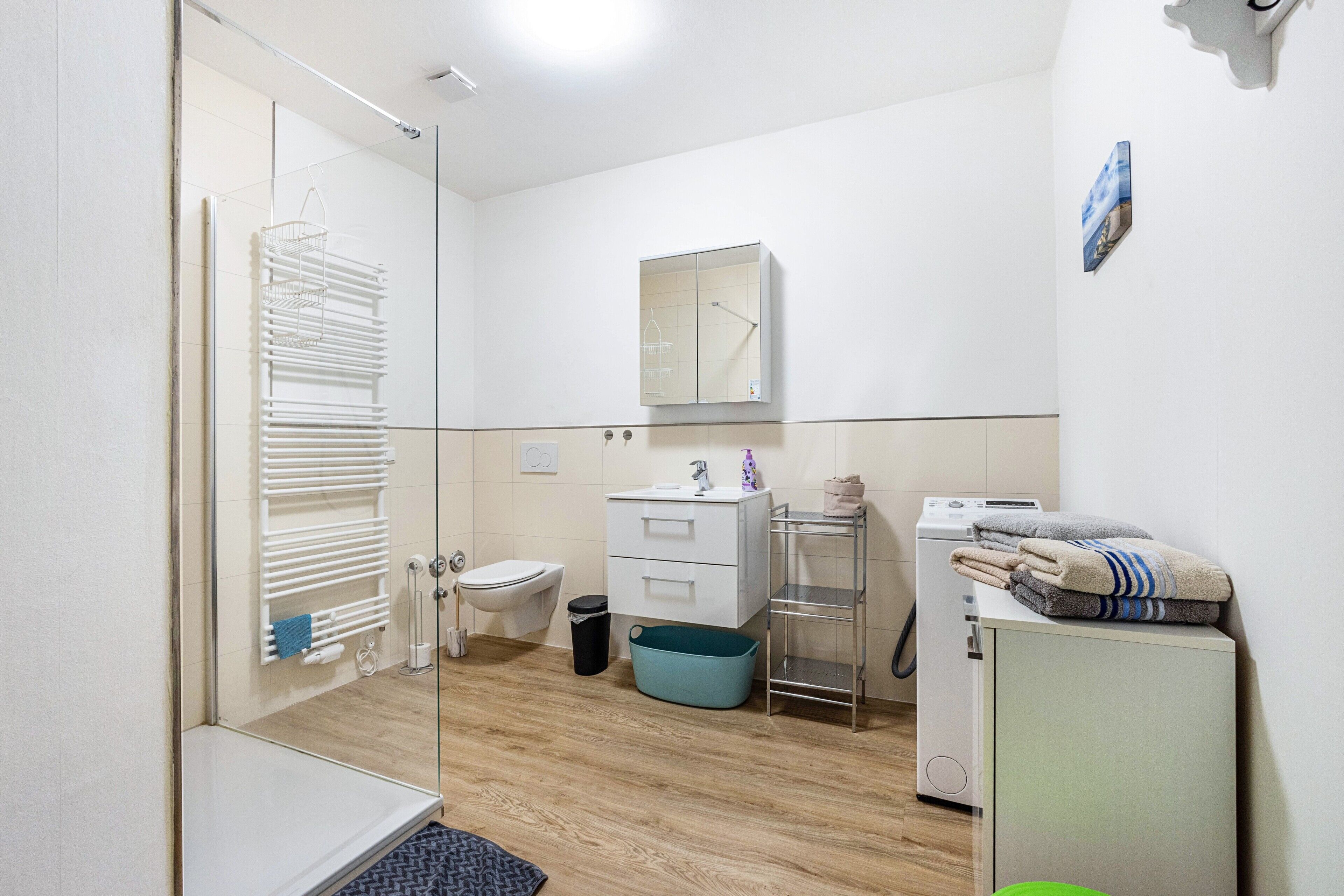 Ein modernes Badezimmer mit Duschkabine aus Glas, Toilette, Waschbecken, Spiegel und Waschmaschine.