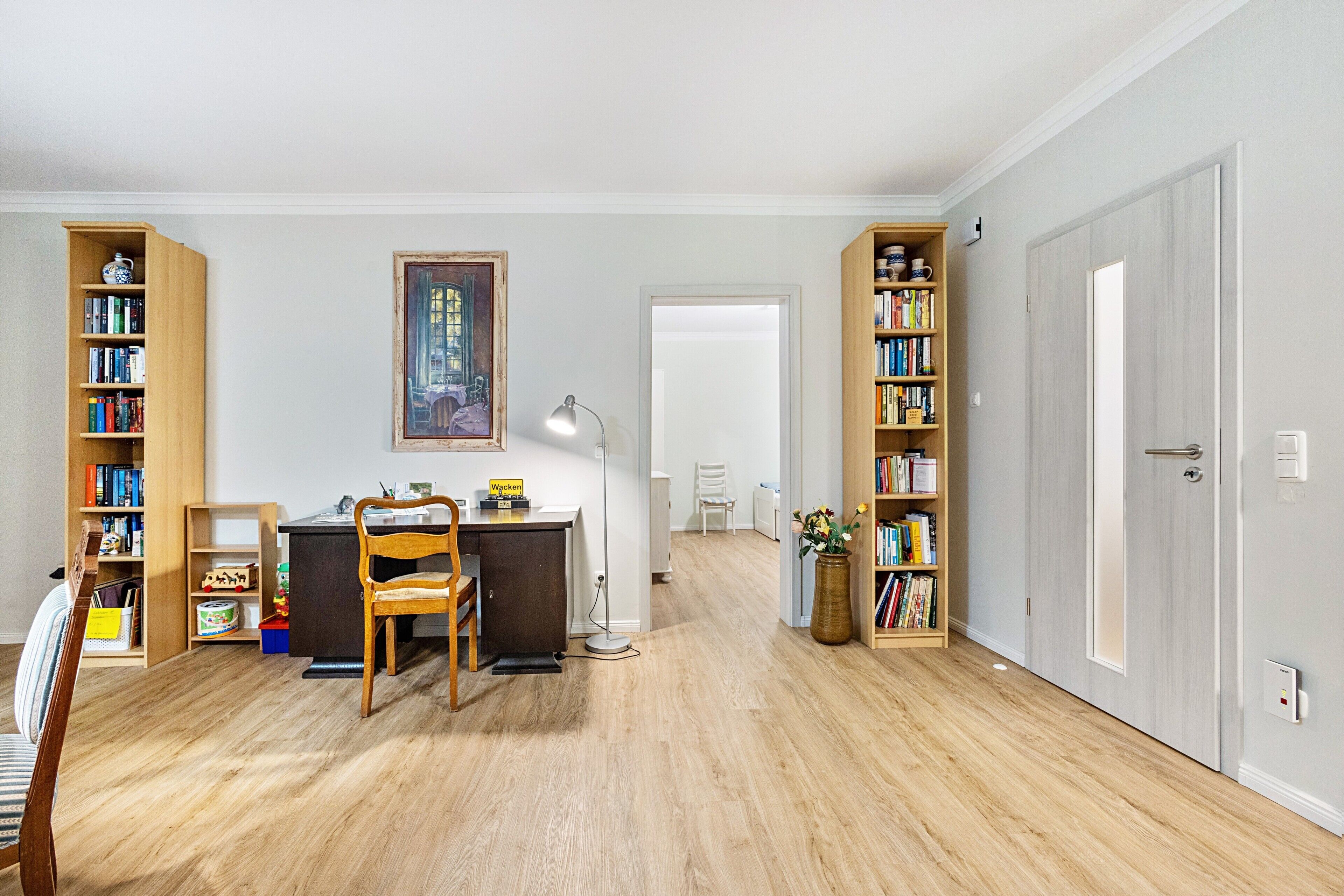 Una habitación con escritorio, silla, estantería y un cuadro en la pared.