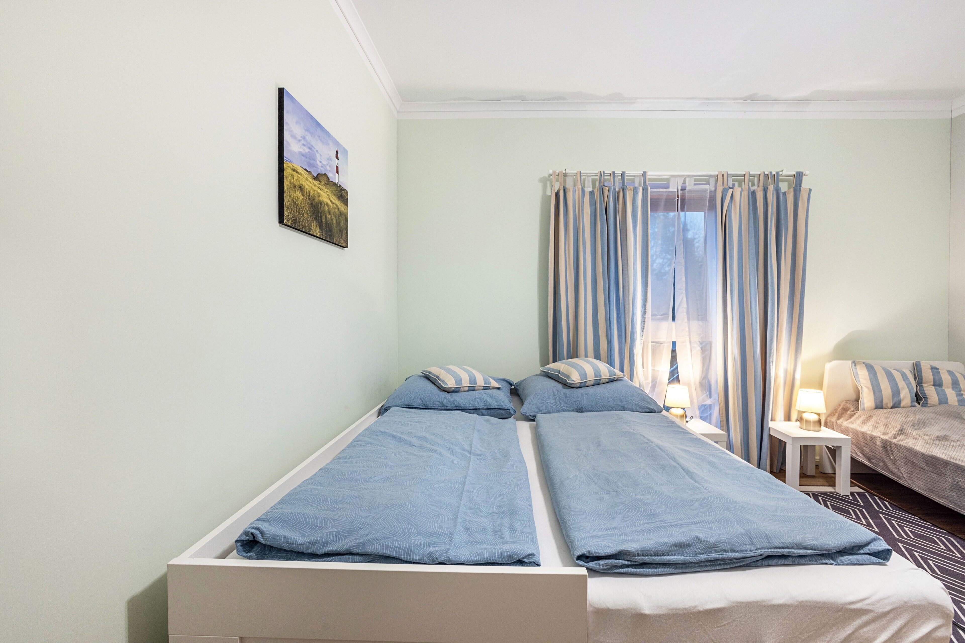 A room with two beds, a small table, a lamp, and a painting on the wall.