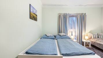 A room with two beds, a small table, a lamp, and a painting on the wall.