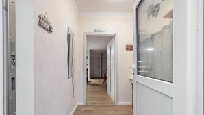 A hallway with wooden flooring, a door with a 'Welcome' sign, and a glass wall with a view.