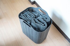 Un panier à linge gris, doté de poignées, posé sur un plancher en bois.