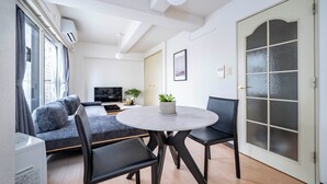 Ein modernes Wohnzimmer mit einem runden Tisch, zwei Stühlen, einem Sofa, einem Fernseher und einer Tür mit Milchglasfenstern.