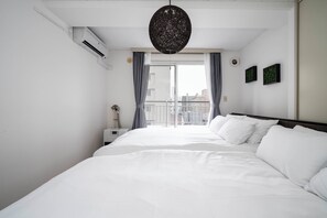 Une chambre d’hôtel avec un grand lit, un ventilateur de plafond, un appareil de climatisation, une table de chevet, une lampe et une vue sur la ville par une fenêtre munie de rideaux.