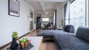 Ein modernes Wohnzimmer mit einem grauen Sofa, einem kleinen Tisch mit einer Vase und Blick auf die Küche und den Essbereich durch ein großes Fenster.