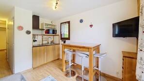 A compact kitchen with a microwave, sink, and wooden cabinets. There is a small dining area with a table and two bar stools. A flat-screen TV is mounted on the wall. - Toison Blanche TBC45 COSY & Mountain 4 Pers (Châtel)