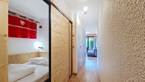 A narrow hallway leading to a bedroom with a wooden wardrobe, a red curtain, and a bed with white linens. - Toison Blanche TBC45 COSY & Mountain 4 Pers (Châtel)