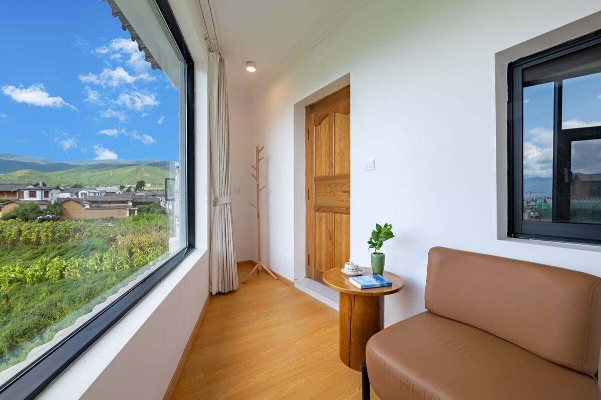 Een moderne kamer met een groot raam, houten vloer, een bruine bank, een klein tafeltje met een plant en een houten deur.