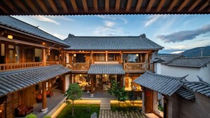 A traditional courtyard with wooden buildings, a central seating area, and a view of the surrounding landscape.