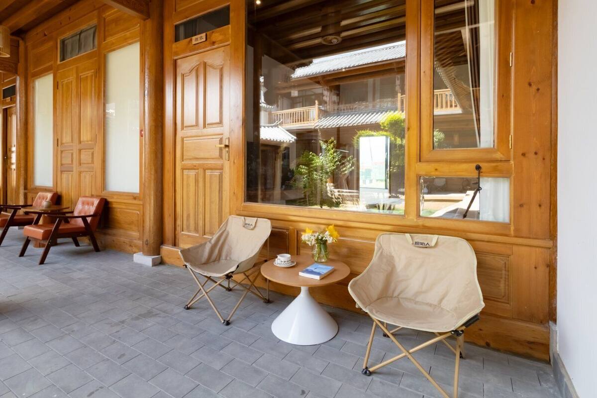 Een houten interieur met twee klapstoelen, een kleine ronde tafel en een raam met uitzicht op een balkon.