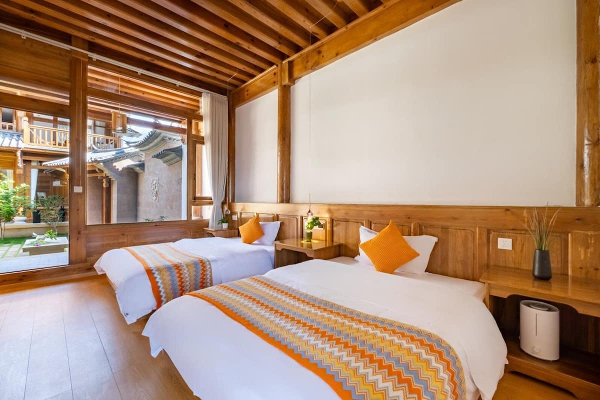 Hotelkamer met twee bedden, houten balken, uitzicht op traditionele architectuur en een klein balkon.