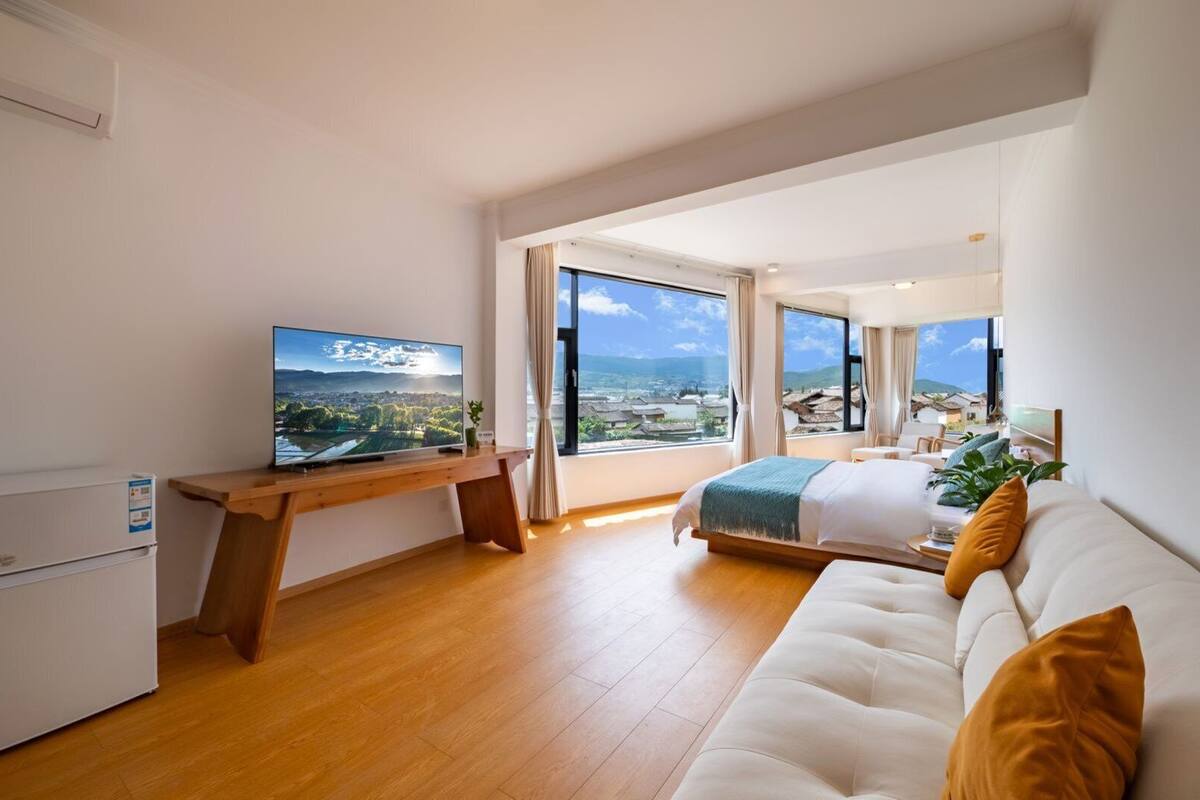 Een moderne hotelkamer met een houten bureau, een groot bed en uitzicht op een stadsbeeld door grote ramen.