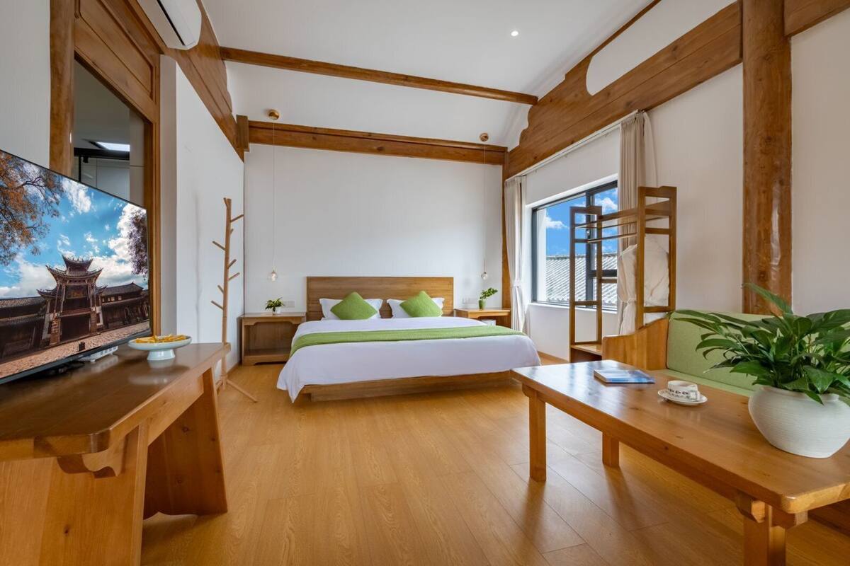 Hotelkamer met een houten bed, een televisie aan de linkerkant, een houten bureau en een groot raam met uitzicht op een traditioneel gebouw.