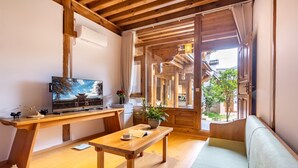 A cozy room with a wooden desk, a television, a sofa, and a view of a traditional building outside.